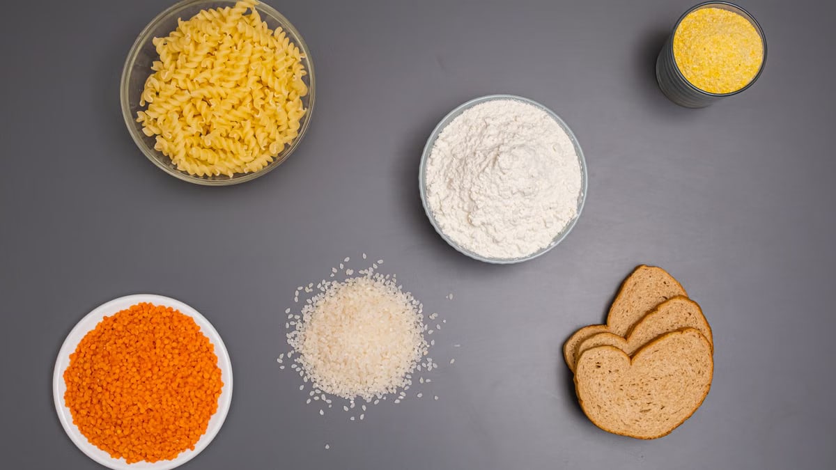 An assortment of dry ingredients including pasta, rice, and bread displayed on a grey background.